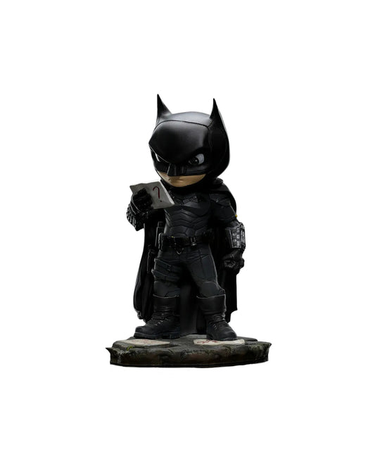 Estatua MiniCo de Batman: figura estilizada del Caballero Oscuro en su traje táctico negro, con capa y máscara, sosteniendo una pista en la mano. Base con papeles y pistas, representando su faceta de detective. Pintada a mano, fabricada en PVC.